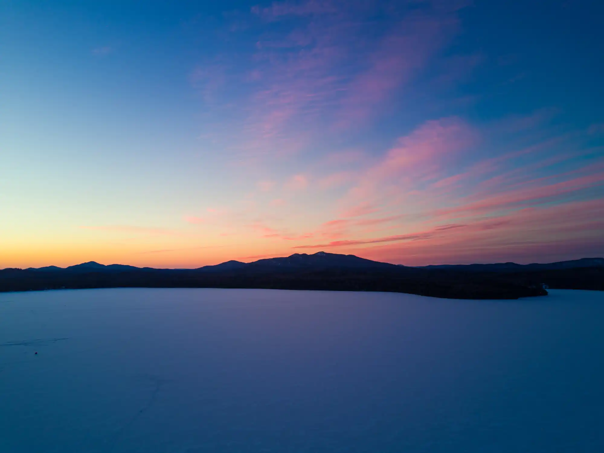An aerial view of Lake Clear with the sunset over Saint Regis Mountain during the winter.
